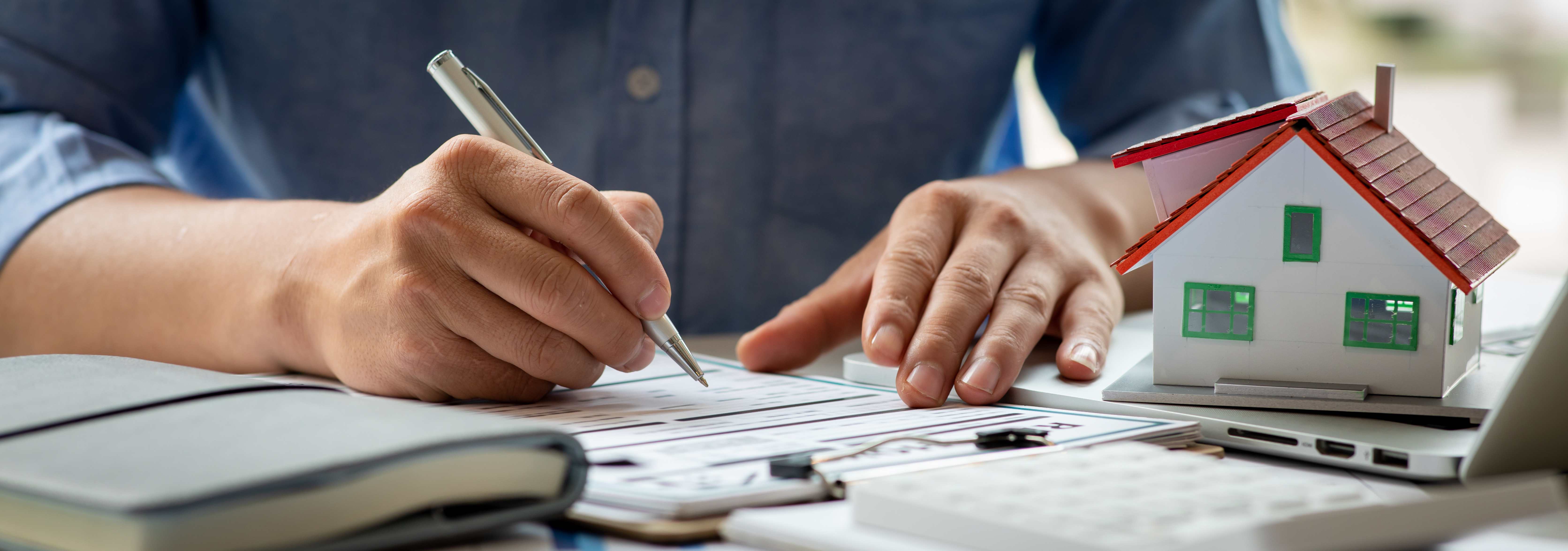 Close up house model with a man signing a remodeling construction agreement