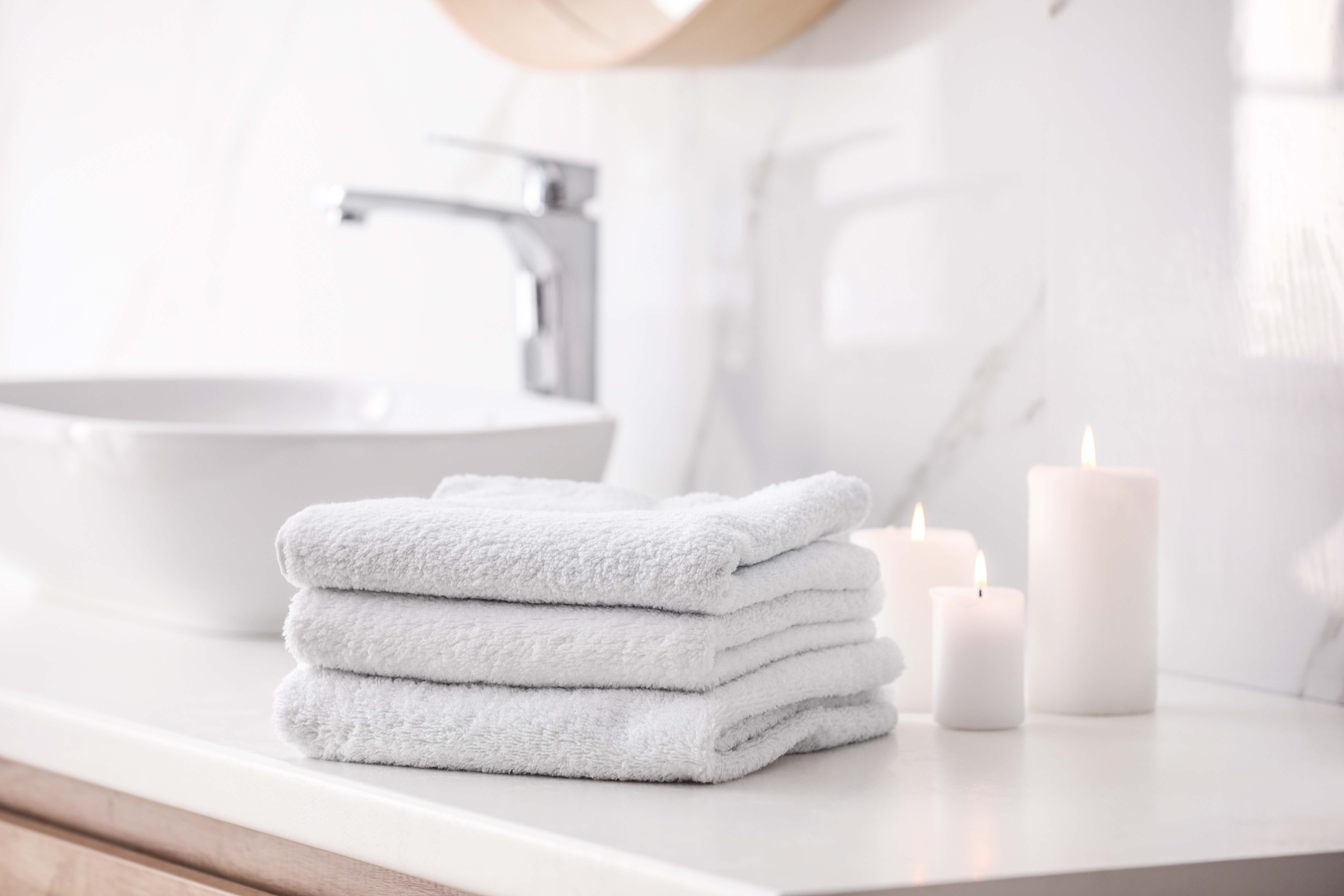 Stack of new white towels and burning candles on countertop in bathroom